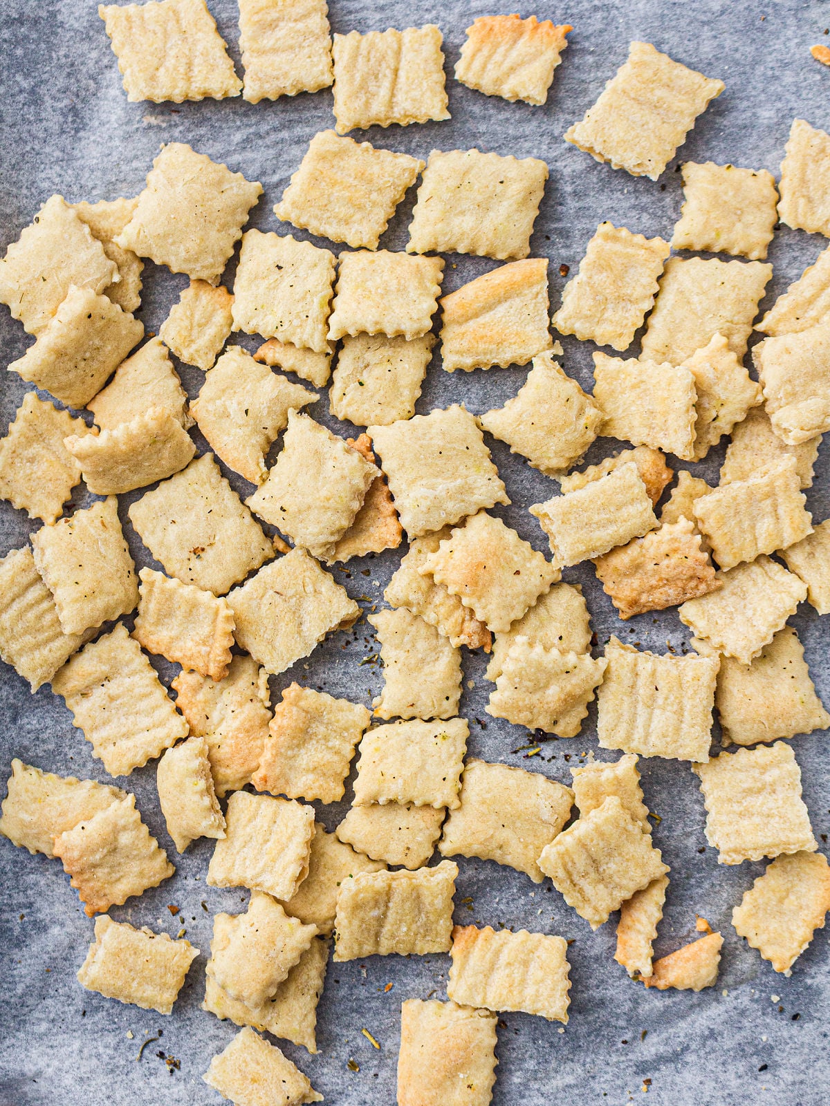 Homemade sourdough discard crackers scattered across parchment paper after baking.