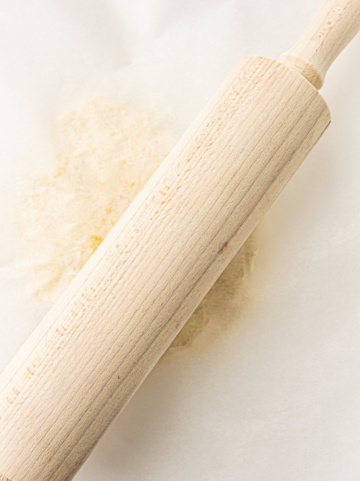 Wooden rolling pin resting on sourdough cracker dough between sheets of parchment paper.
