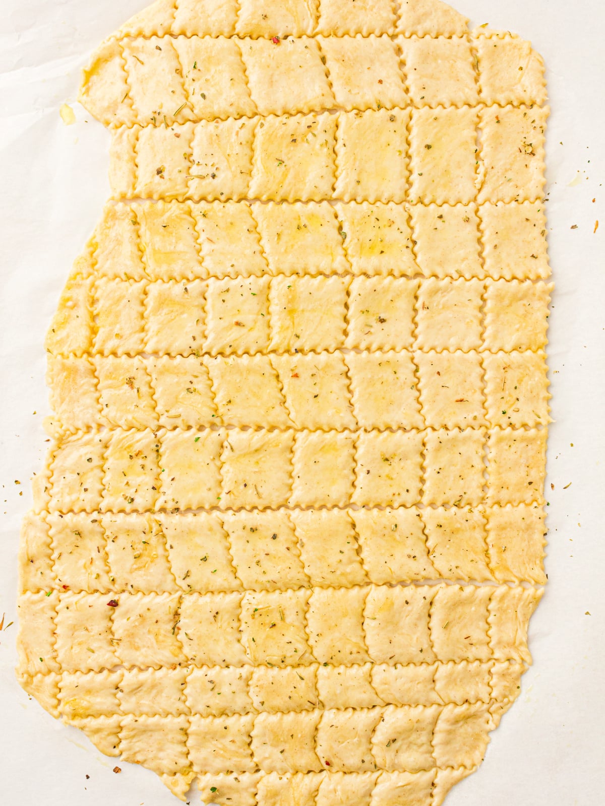 Seasoned sourdough cracker dough cut into small rectangles with fluted edges.